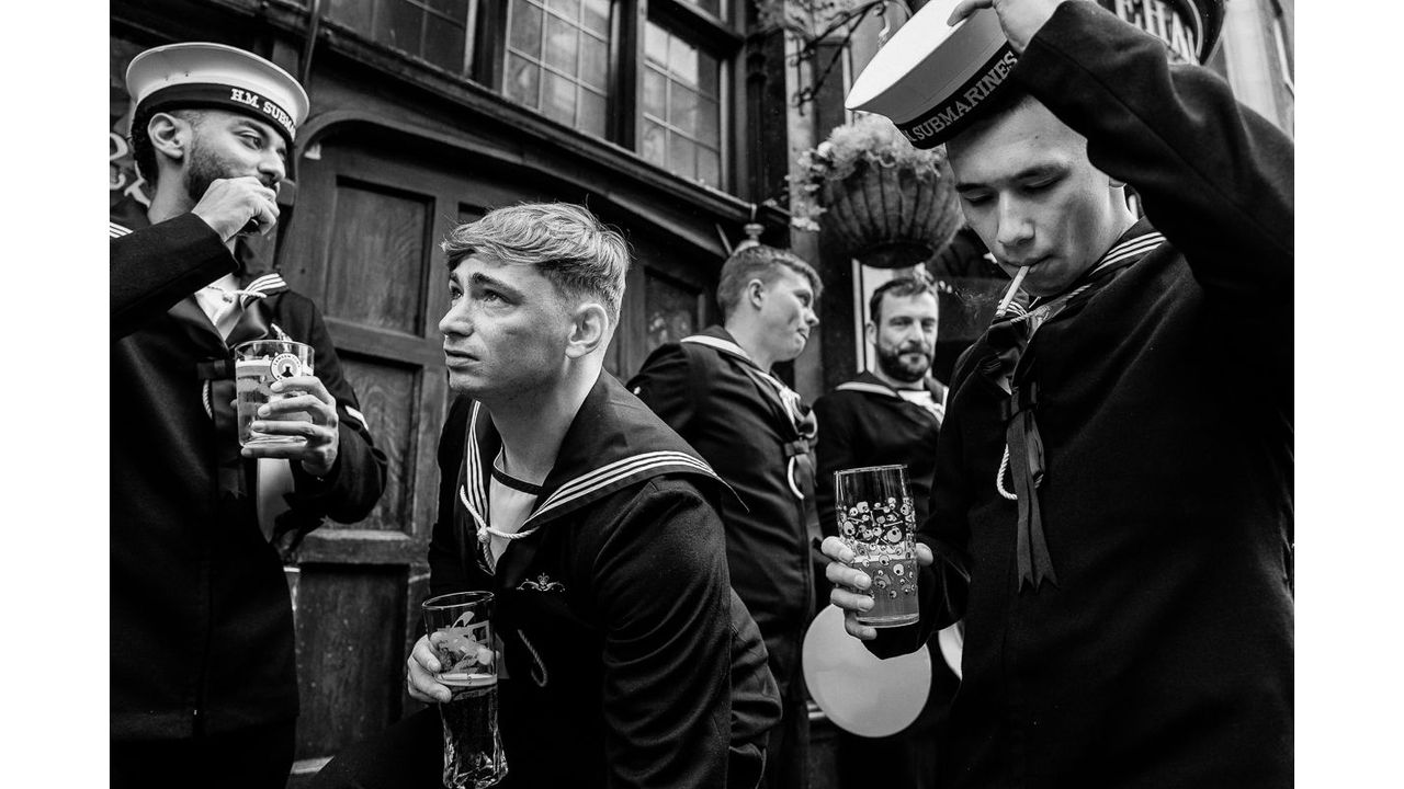 Black-and-white photo of five sailors in uniform drinking and smoking outside a building