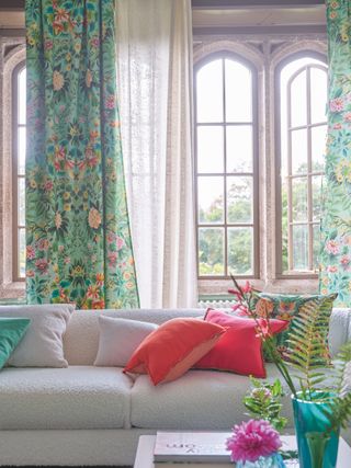 spring style living room with boucle couch, spring floral drapes and matching pillows, airy drapes, window open, vase with flowers, bright plain pillows