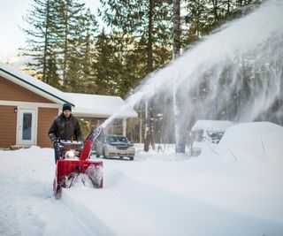 Man using snow blower machine to clear driveway