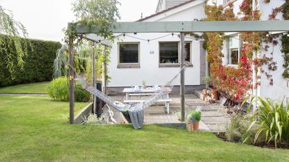 A garden with a tidy lawn and flowerbeds, wooden deck, raised bed edging, and plank path, and grey fence and sun loungers