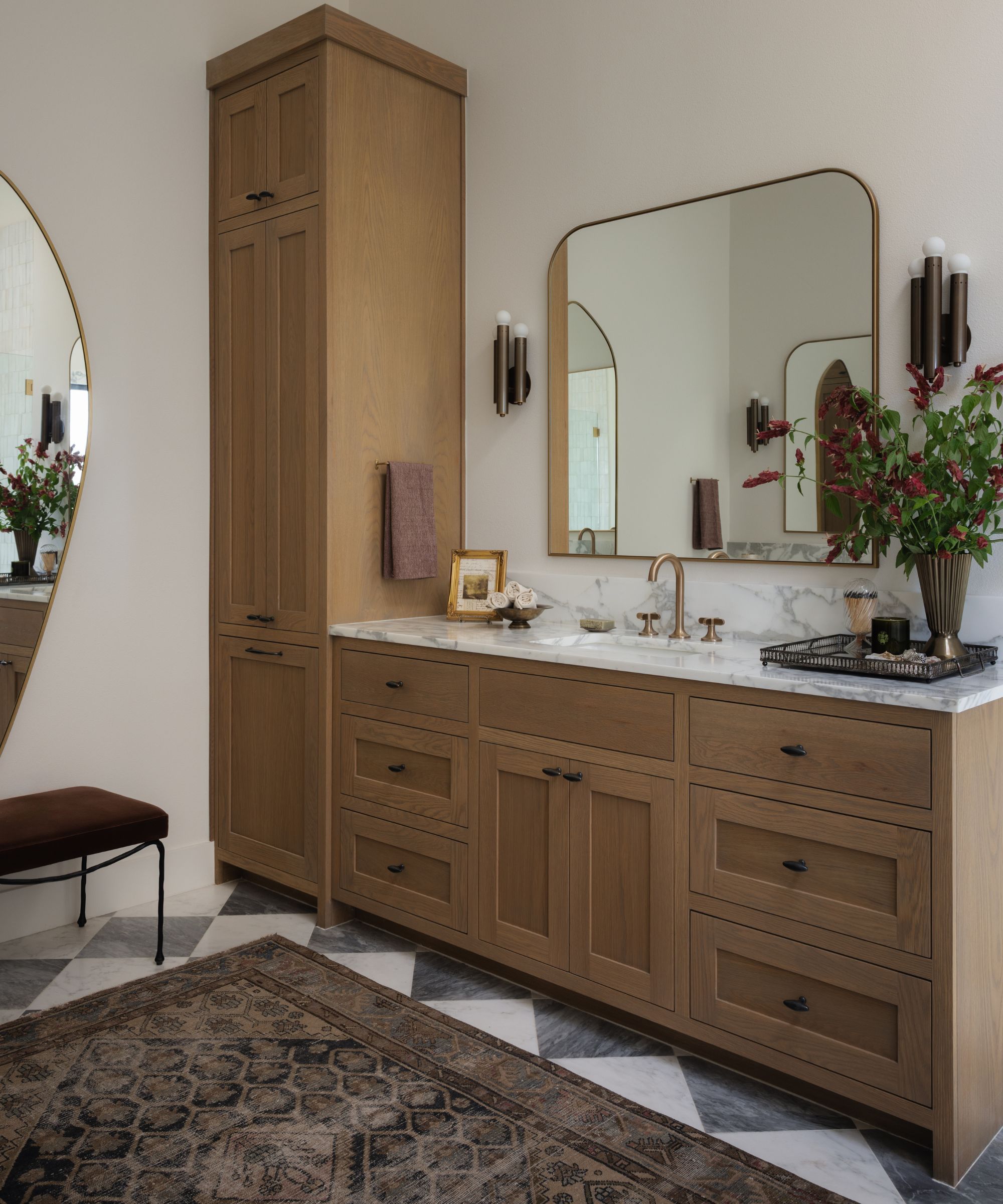 a warm neutral primary bedroom with oak cabinetry and vanity with a marble checkerboard floor and vintage turkish rug underfoot