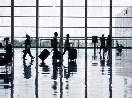 People walking with suitcases past a window at an airport.