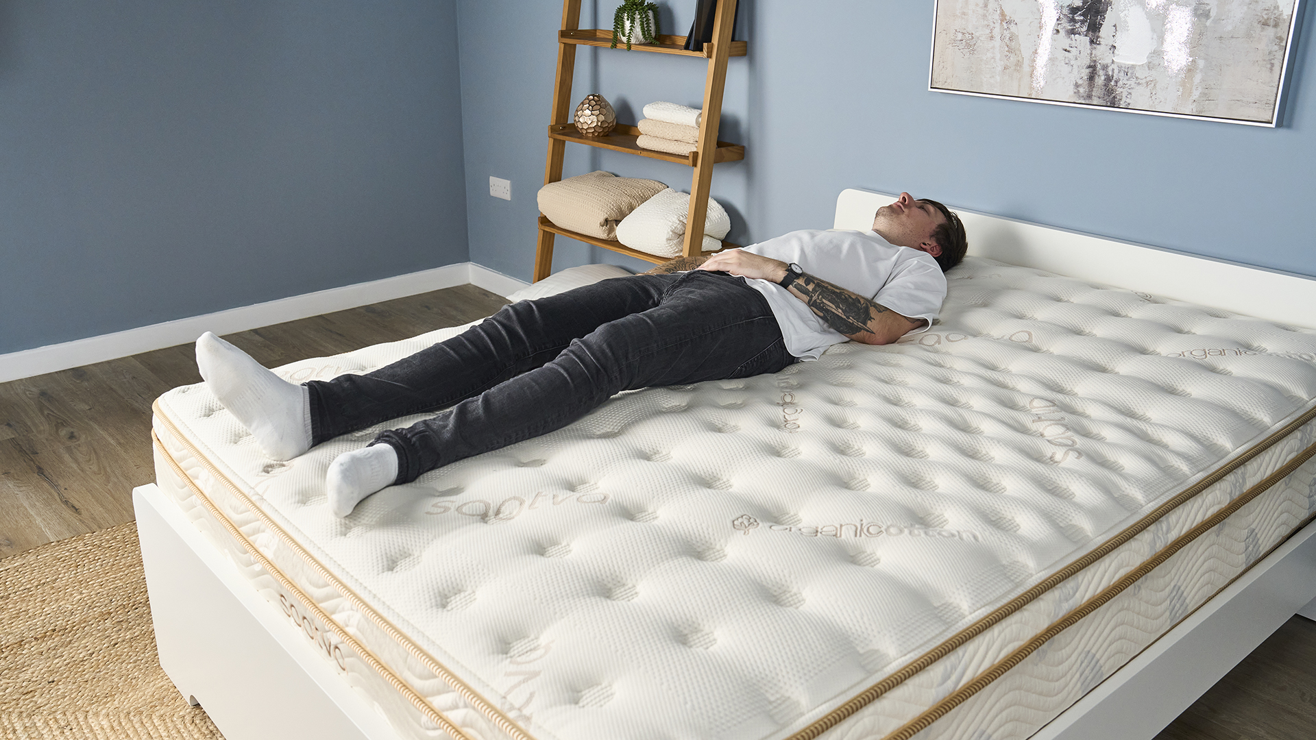 A man lies on his back on the Saatva Classic Mattress in a bedroom with blue walls