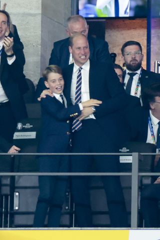 Prince William and Prince George wearing suits and ties and hugging each other at a Euros match