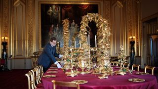 An employee poses by the table in the State Dining Room which has been decorated for the Christmas period with silver-gilt pieces from the Grand Service