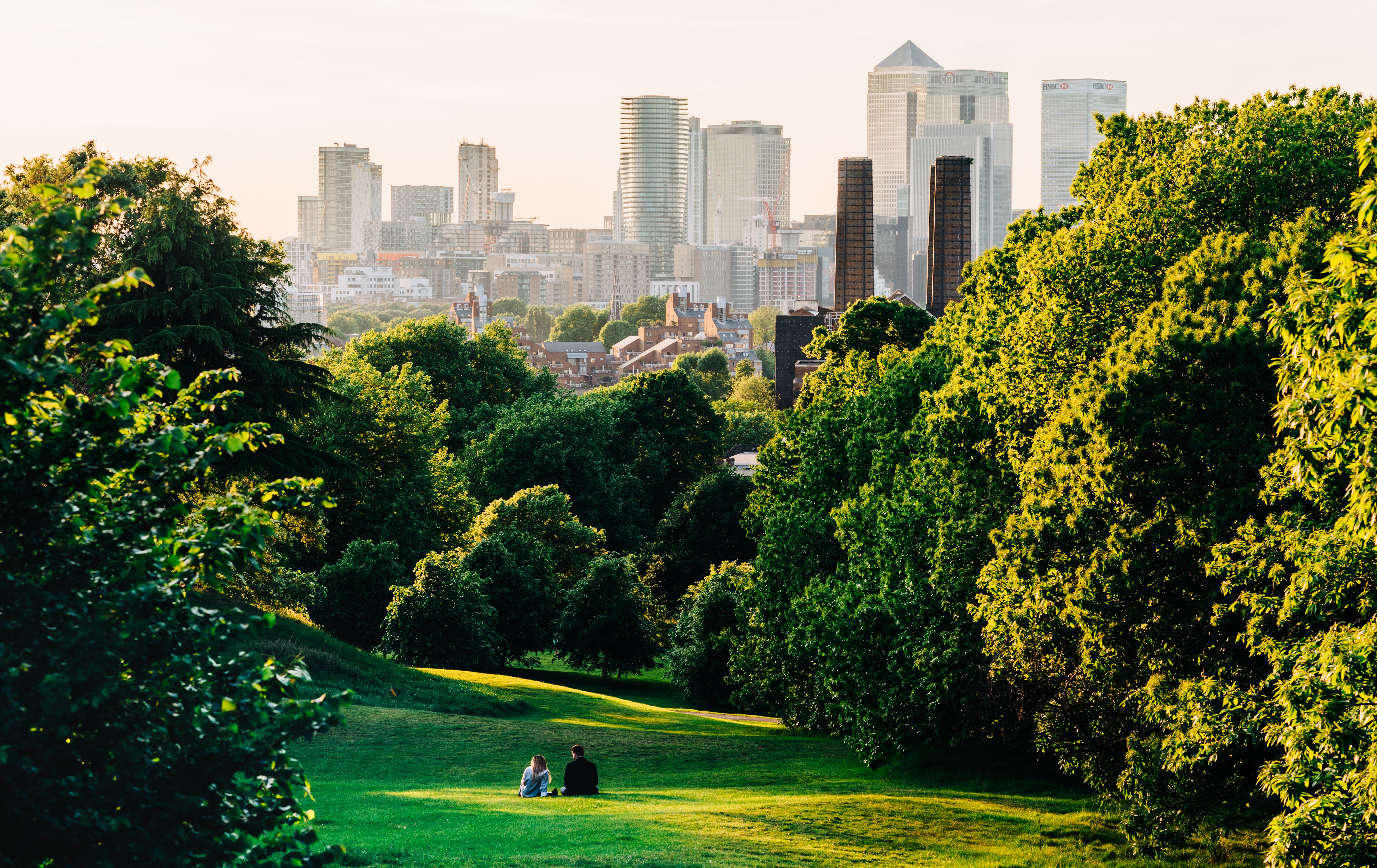 Two people sitting in the middle of Greenwich Park overlooking Canary Wharf