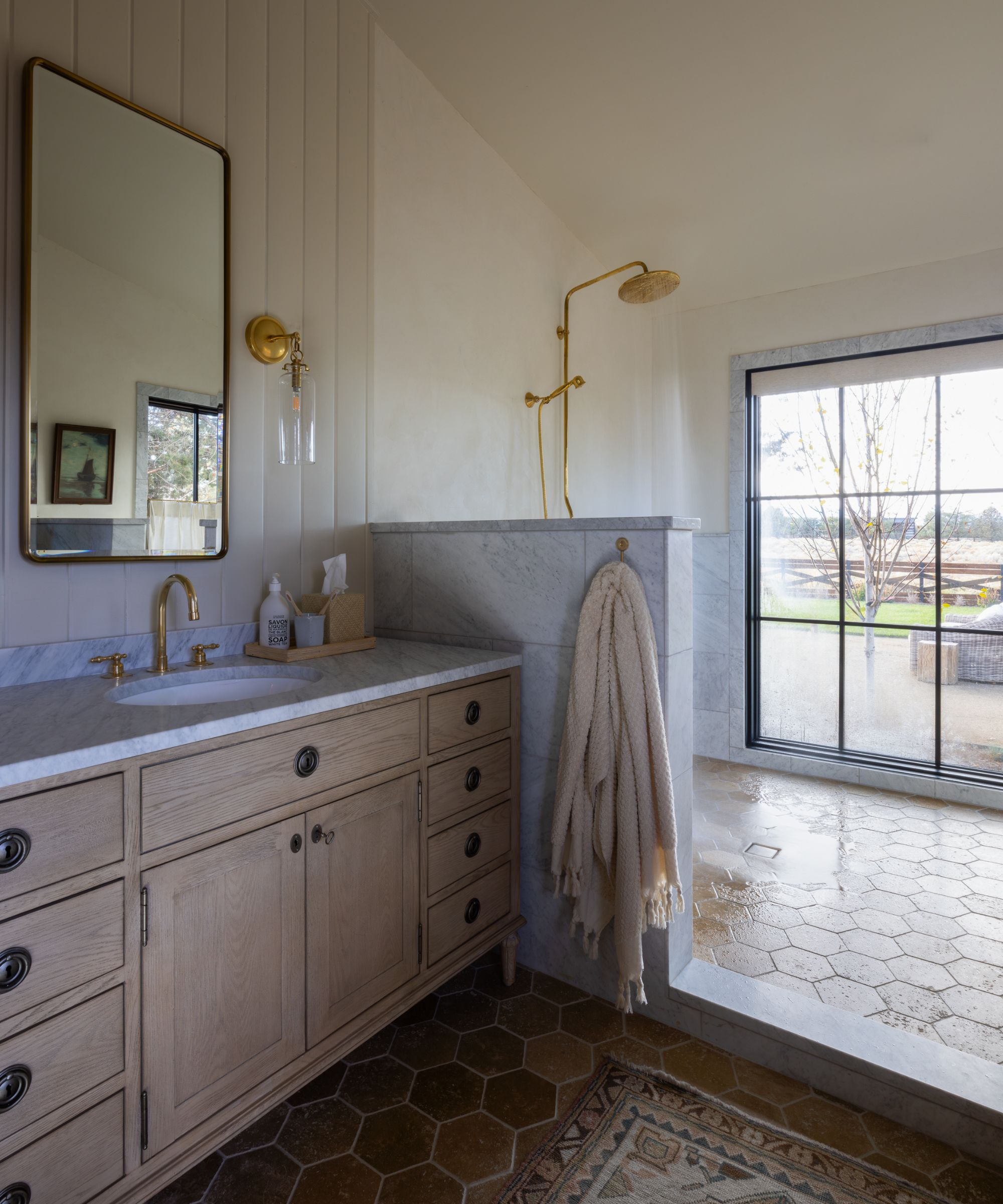 Large light filled bathroom with a marble divider between the walk in shower and vanity area