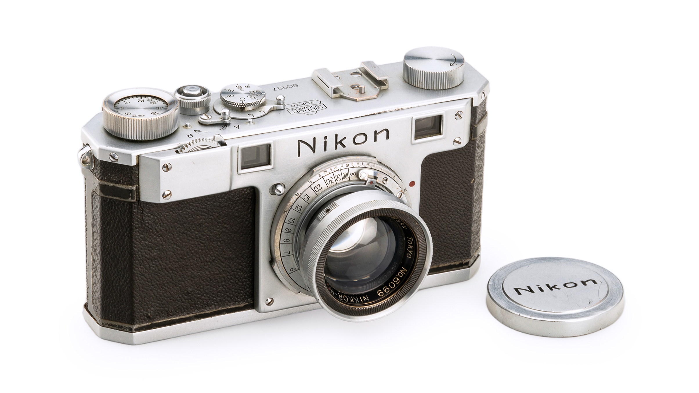 Vintage Nikon camera with a silver body and leather grip, alongside its round lens cap, set against a white background