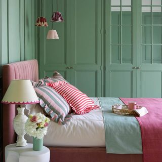 green and pink bedroom with bed and frilly cushions and bedside lamp