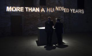 Two men stand over a lit display. The words "MORE THAN A HUNDRED YEARS" is illuminated on the wall