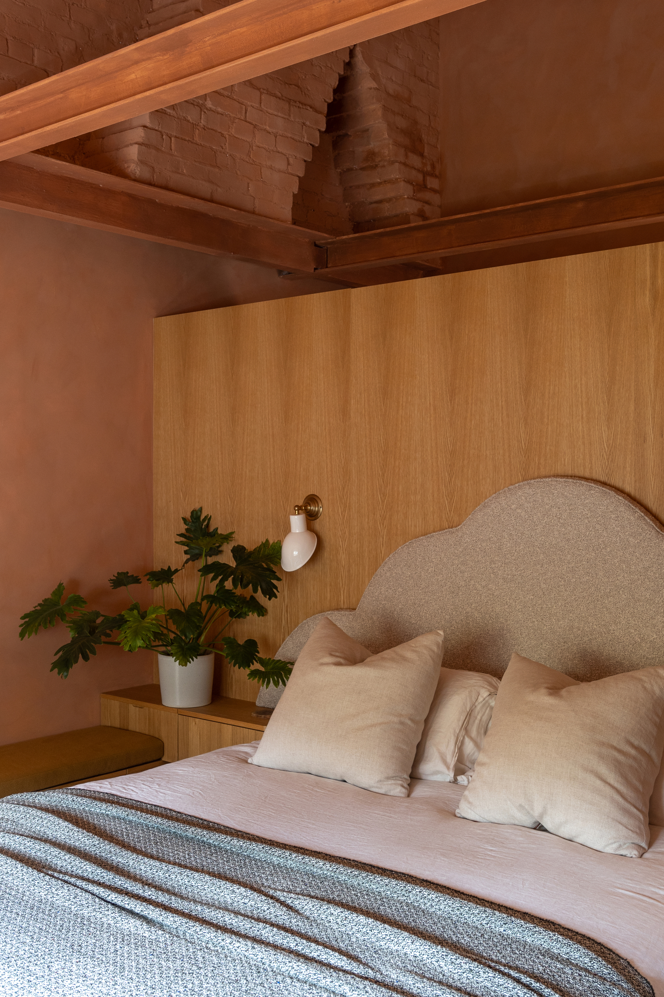 Bedroom with extended wooden headboard, terracotta walls and pink and blue bed linen