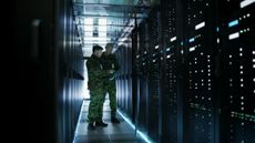 Two military personnel stood inside a moodily-lit data center.