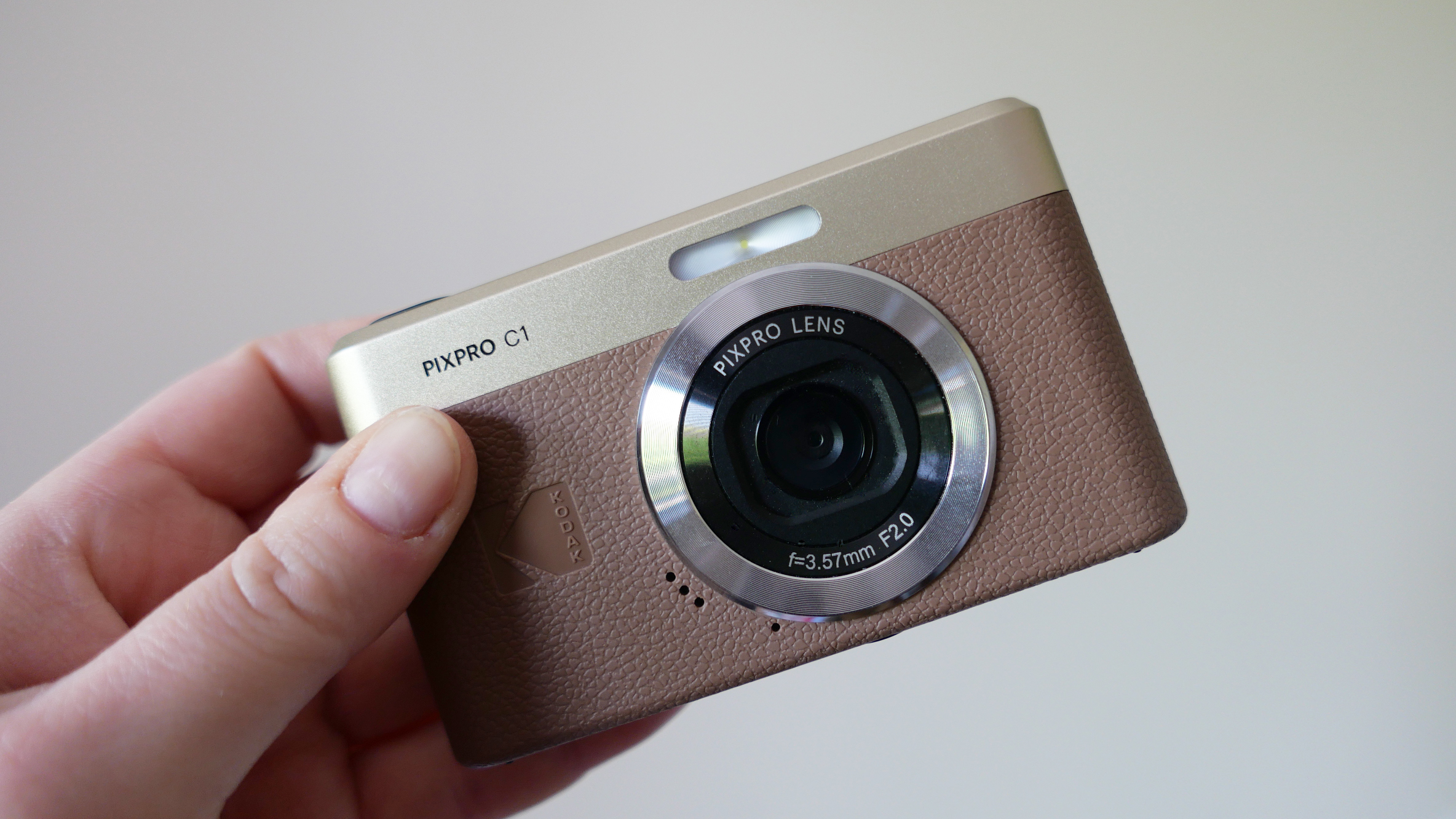 A person holding a Kodak Pixpro C1 camera with a stylish design, showcasing its lens and textured body in a well-lit setting