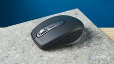 A photo of the Logitech MX Anywhere 3S mouse on a stone surface with a blue wall in the background.