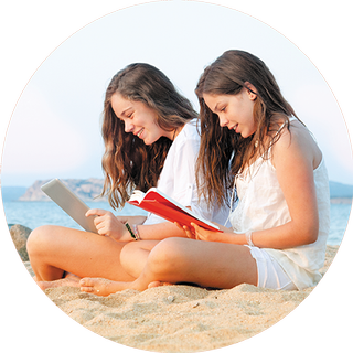 Image of two girls sitting on the beach reading their books