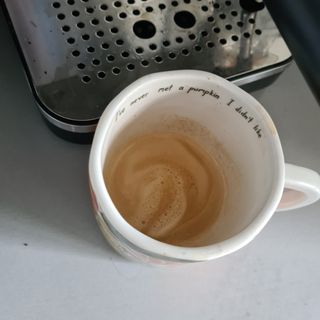 White coffee mug half-filled with coffee next to a coffee machine on a white counter-top