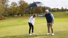Holding an umbrella over a player while they putt