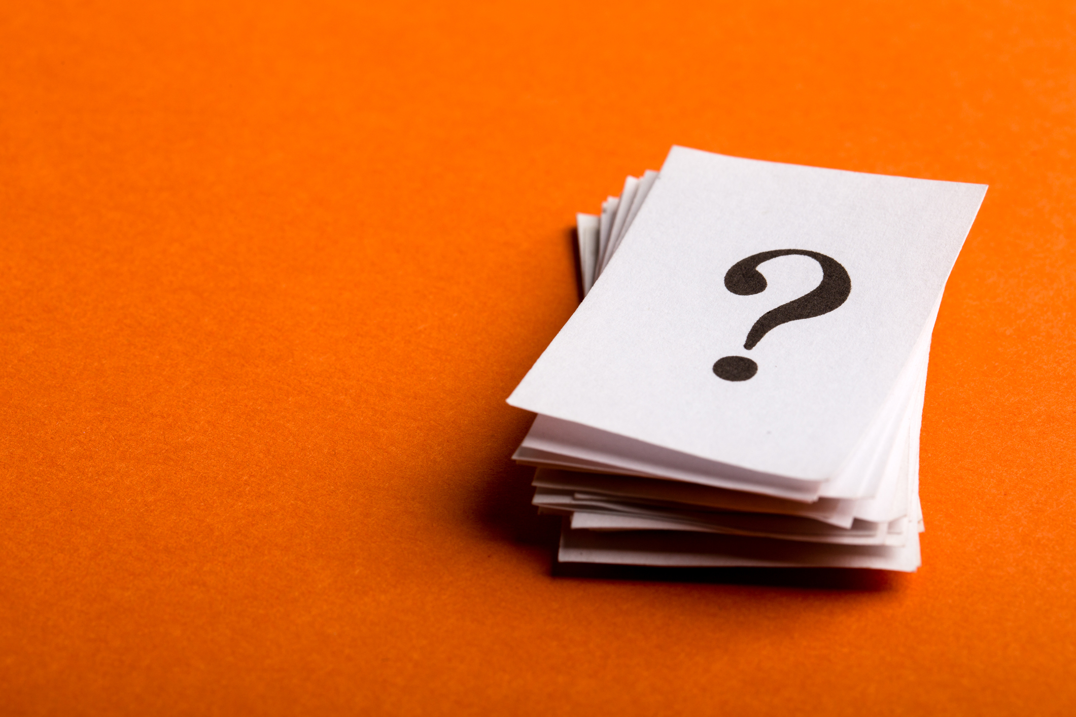 question mark on a stack of white papers against orange background