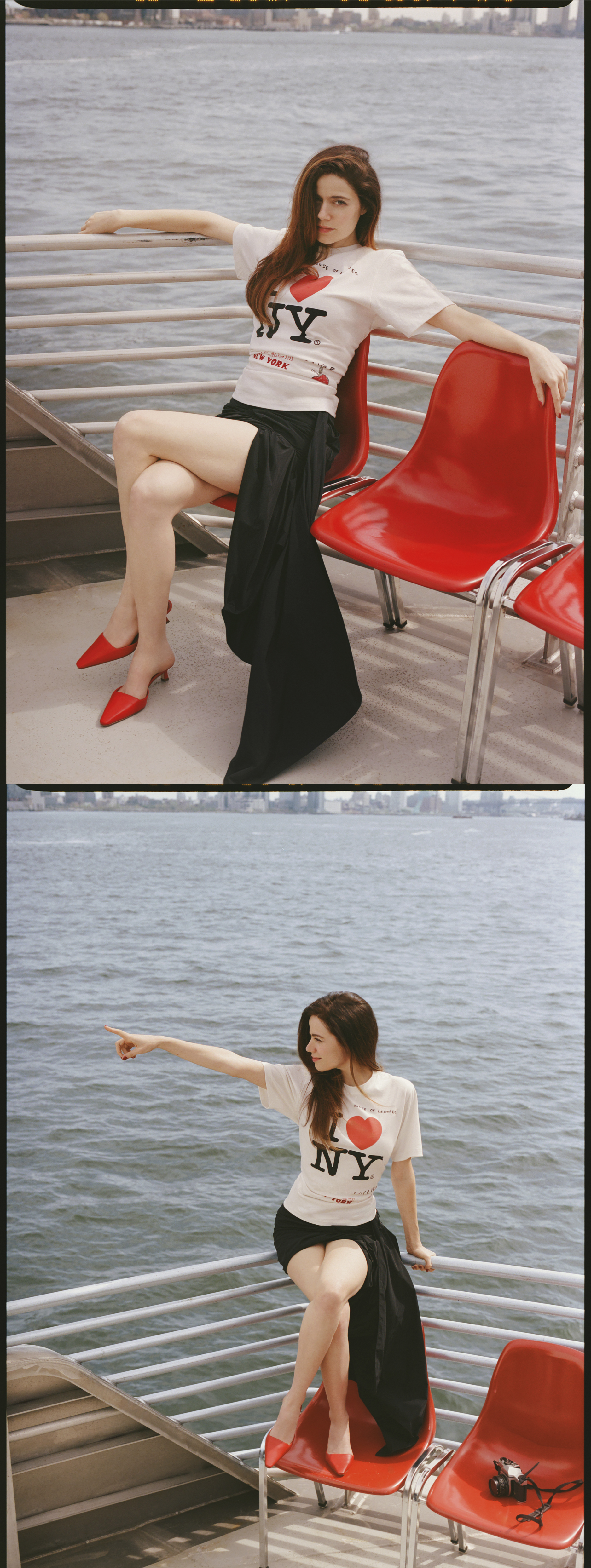 Molly Gordon sitting outside on a ferry boat. She is seated in a red plastic chair, her arms perched on the railing behind her. She is wearing an "I Love NY" T-shirt with a black skirt and red heels.