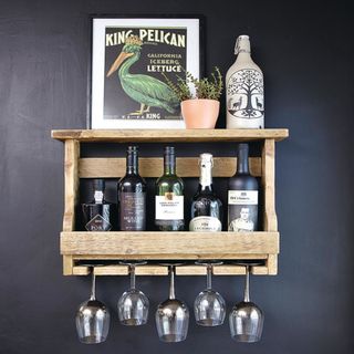 wooden shelving with bottles of alcohol and glasses against a black wall