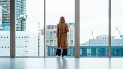 Woman looks out window of office building.