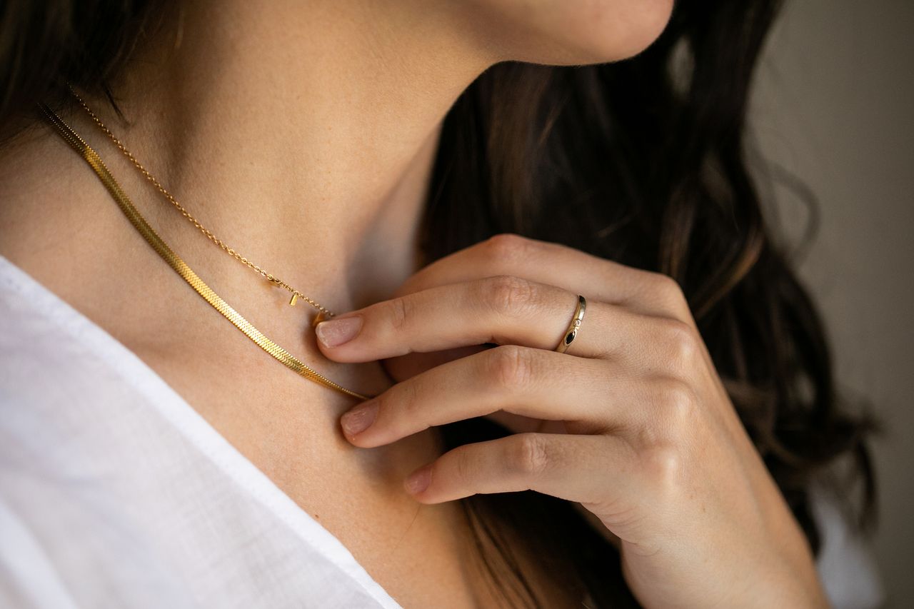 A close up of a woman&#039;s neck with two minimalist gold necklaces along with her hand with a small, gold ring on.