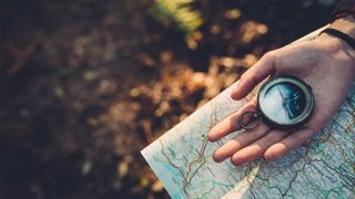 Person's hand holding a compass on top of a map