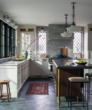 Tudor revival kitchen with a black and gold island, white cabinets, and a grey marble backsplash