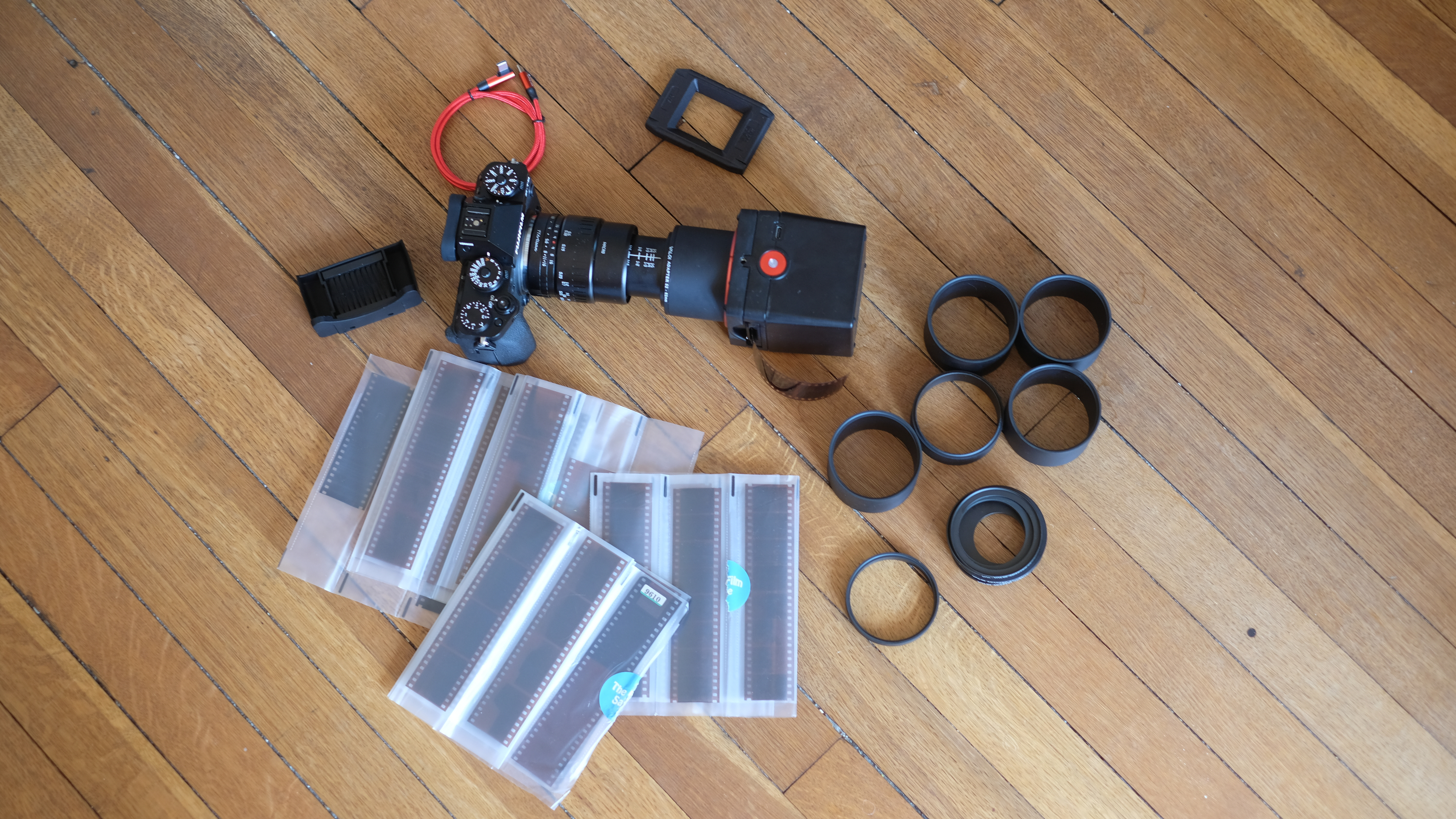 Photograph of the Valoi Easy35 V2 film scanner kit laid out on the floor, including camera, scanner, extension tubes, holder, dust brush, USB cable and film negatives