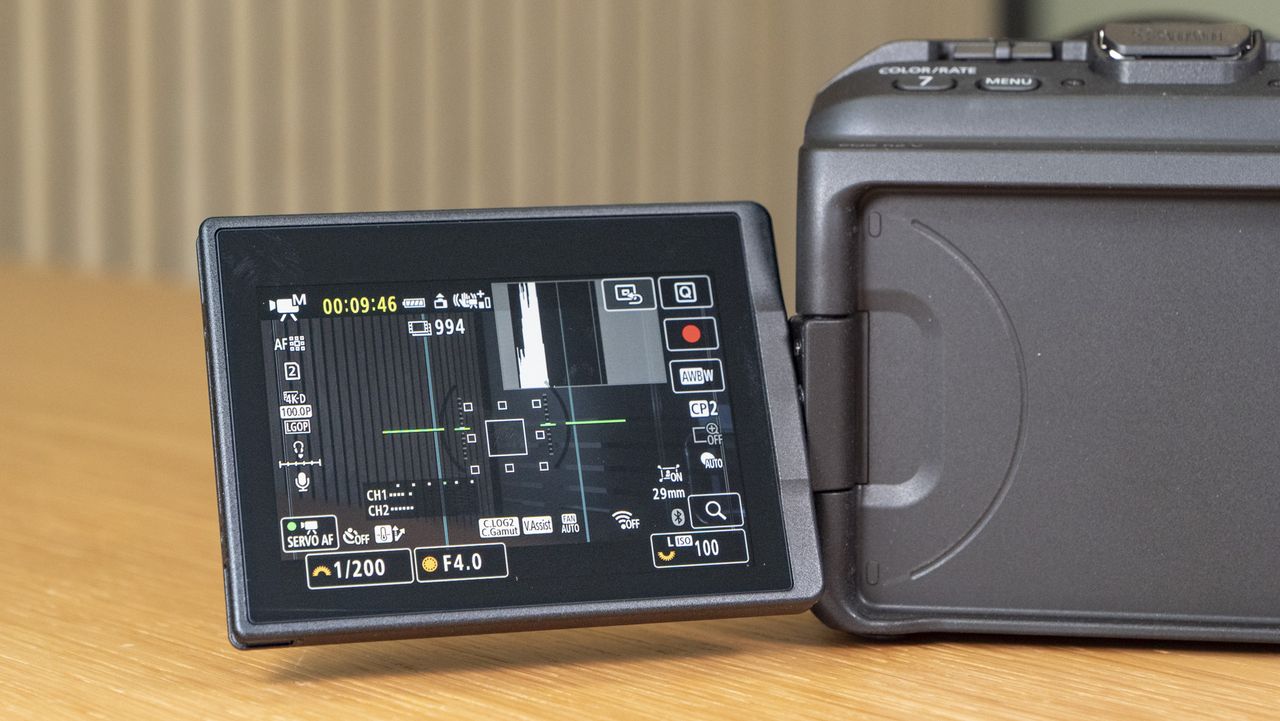 Rear of the Canon EOS R6 V mirrorless camera, it's on a wooden table with a pine-slatted backdrop, the screen is flipped out to the side