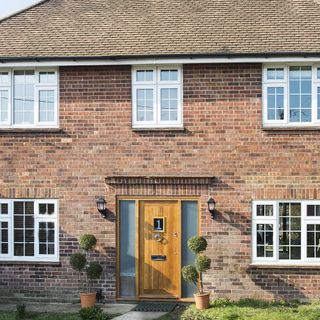 brick wall with white window and front door with shrubs