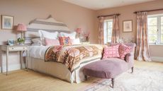 Pale pink bedroom with striped upholstered large headboard. Layered bedding, throws and patterned curtains make it look cozy but bright.