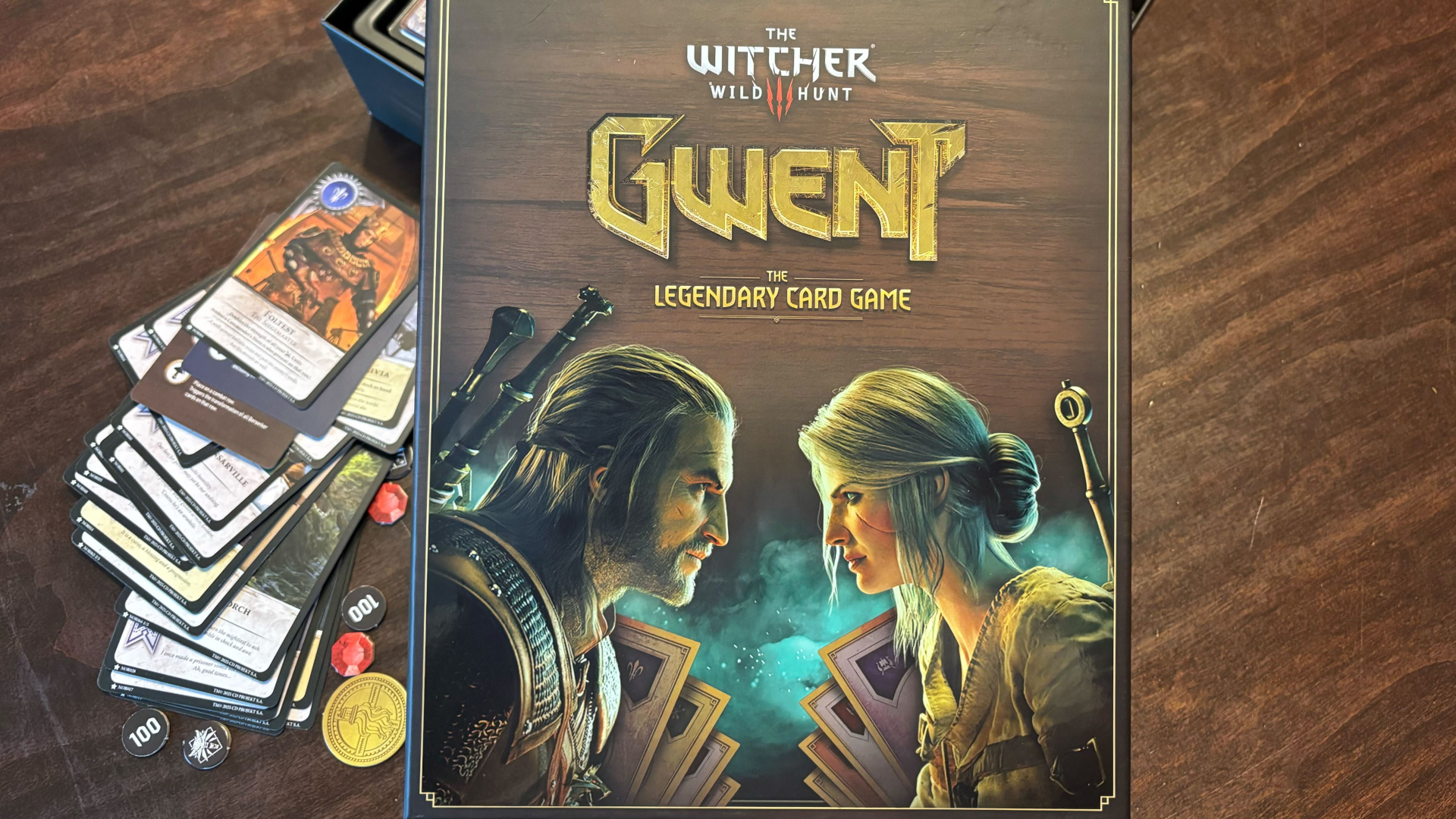 Gwent: The Legendary Card Game box on a wooden surface beside assorted cards and tokens