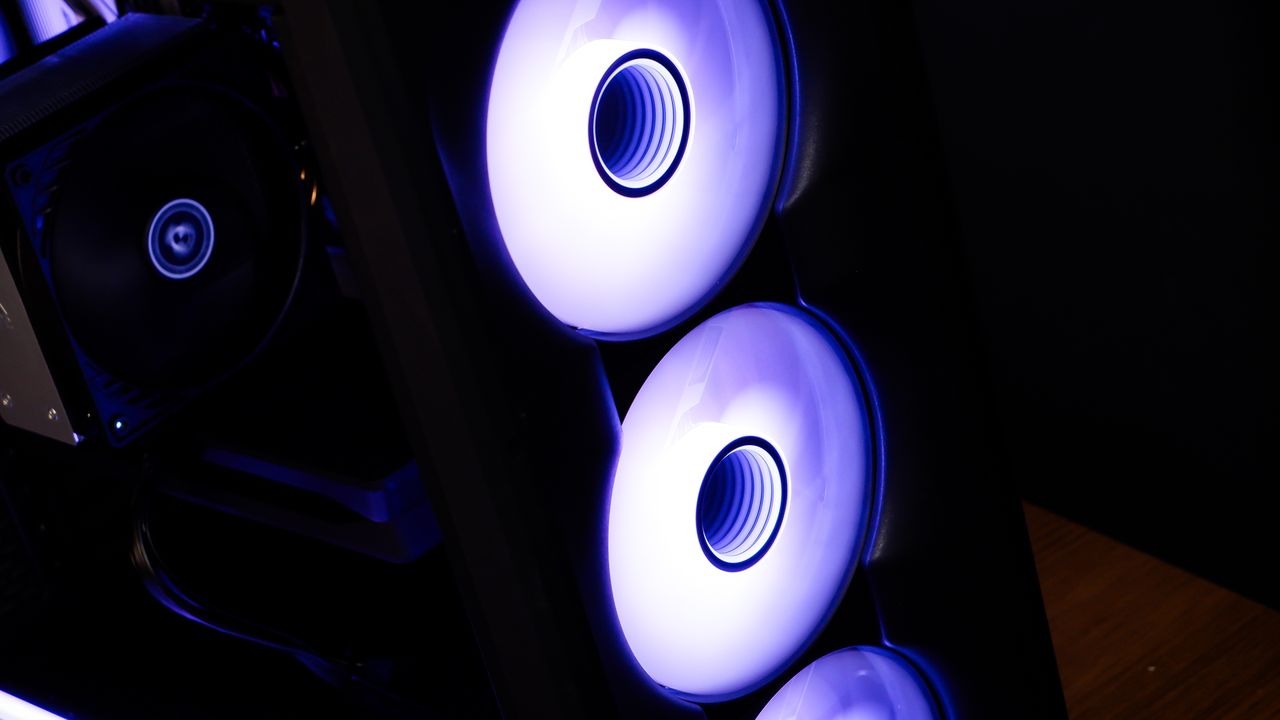 A gaming PC sat on a desk with purple RGB lighting on the fans and light bar enabled.