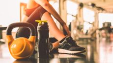 A person sat on the floor at the gym with their gym water bottle and a kettlebell