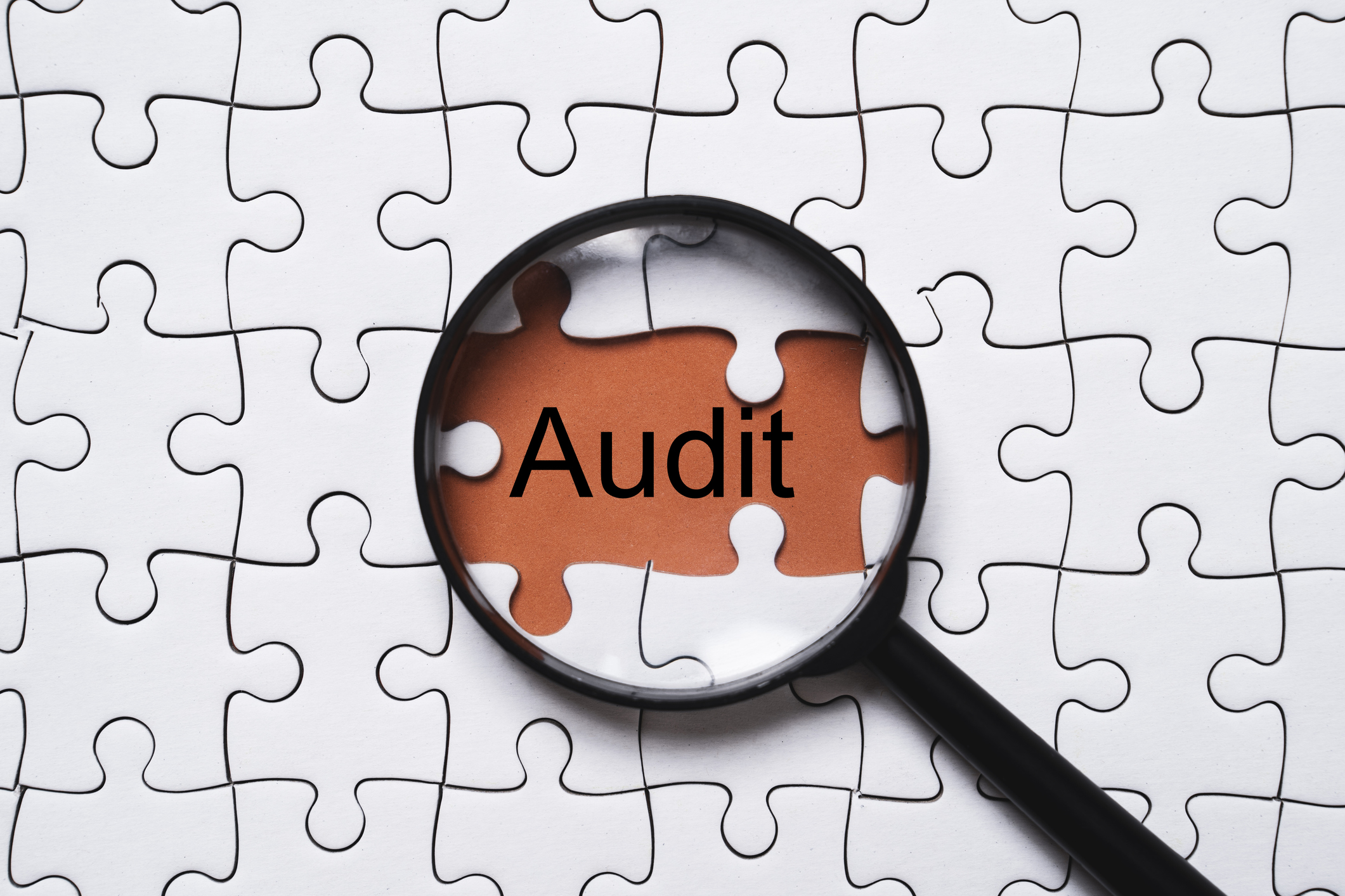 The word "audit" beneath a magnifying glass in a jigsaw puzzle 