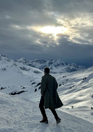 Man in coat on snowy mountain with moody sky