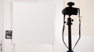 A Canon camera set up on a tripod pointing at a large sheet of white card with a color calibration device next to it