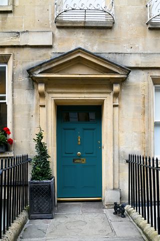 Grand front door with decorative limestone surround and teal door with brass details