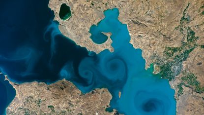 An astronaut photo of a deep blue lake in Turkey with milky light blue swirls spinning in the water