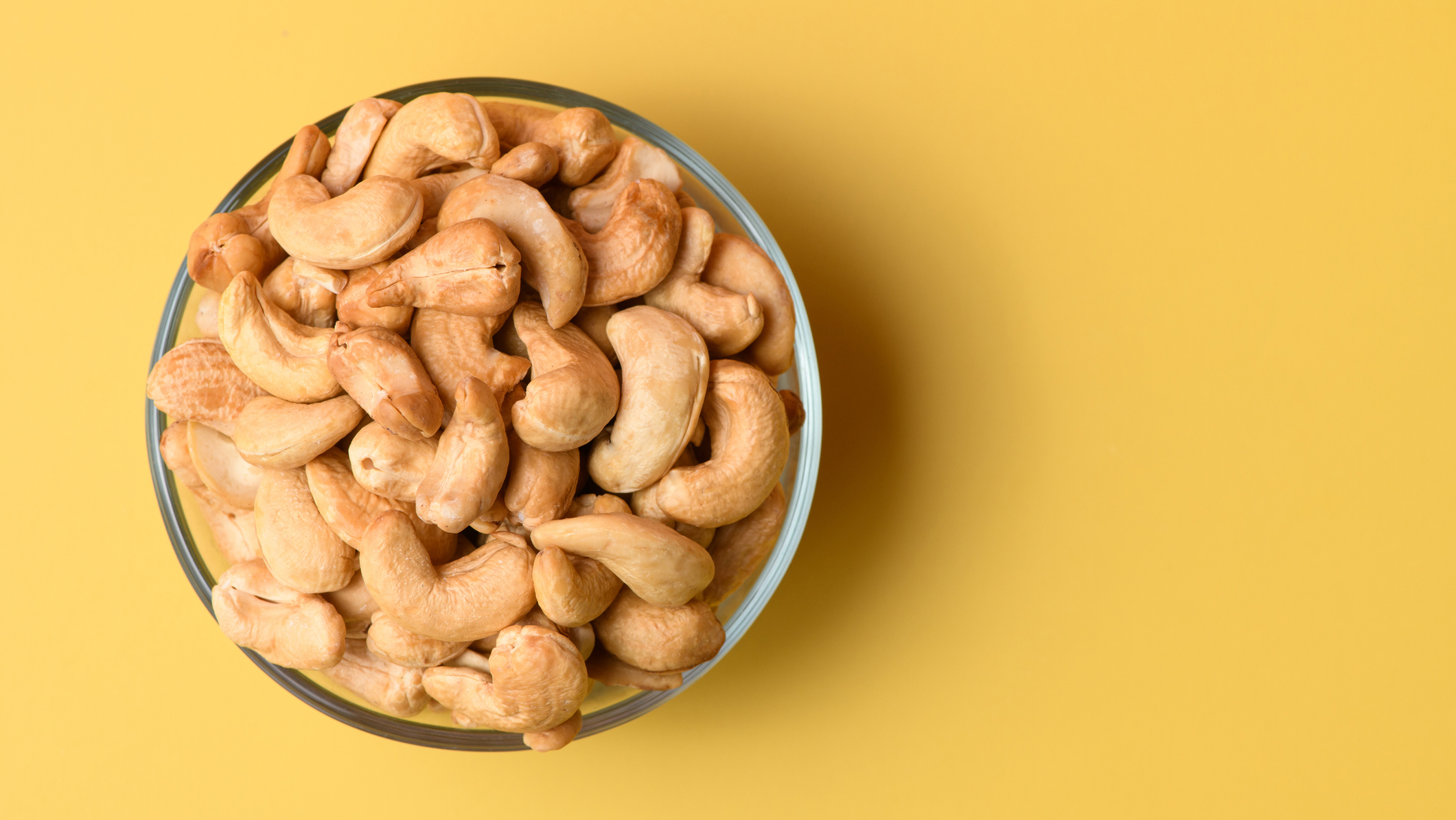 A bowl of cashew nuts on a yellow background