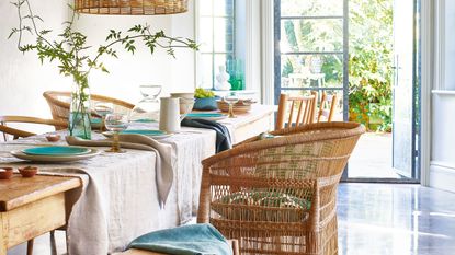 Wooden dining table with beige linen tablecloth and wicker chairs