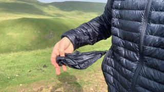 A hiker's hand pulling the stuff sack out of her blue down jacket pocket