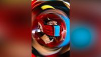 Race car driver in a red helmet fastening the chin strap, with a swirling motion blur effect around the image
