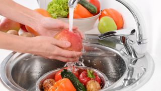 Fruit and vegetables being rinsed under a running faucet