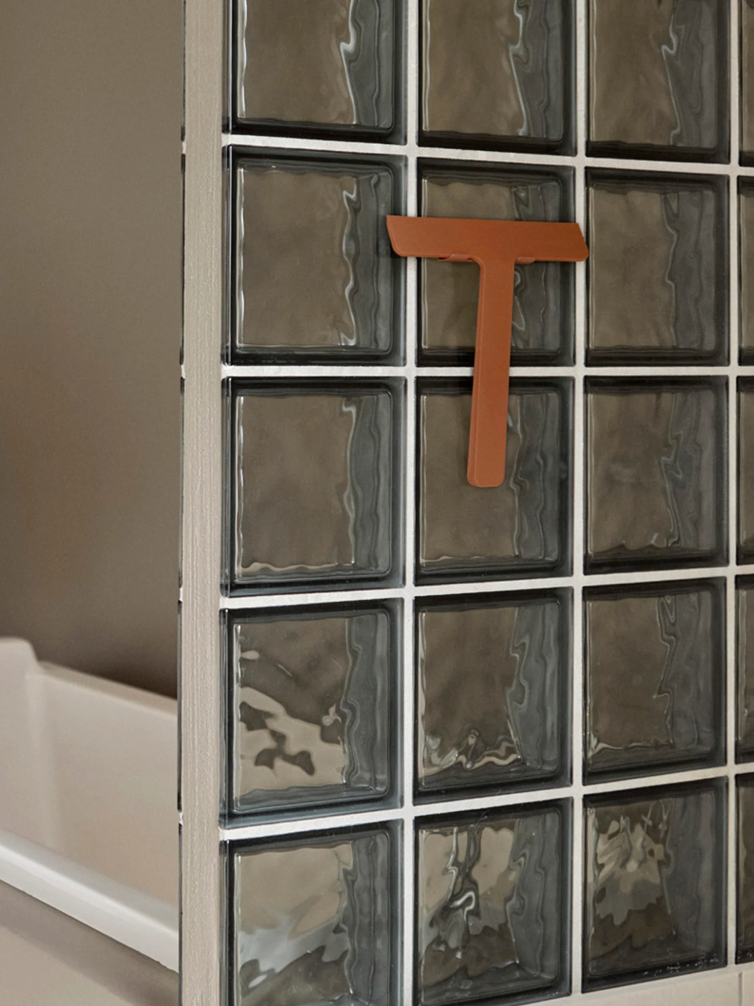 A terracotta-colored squeegee on a glass block wall
