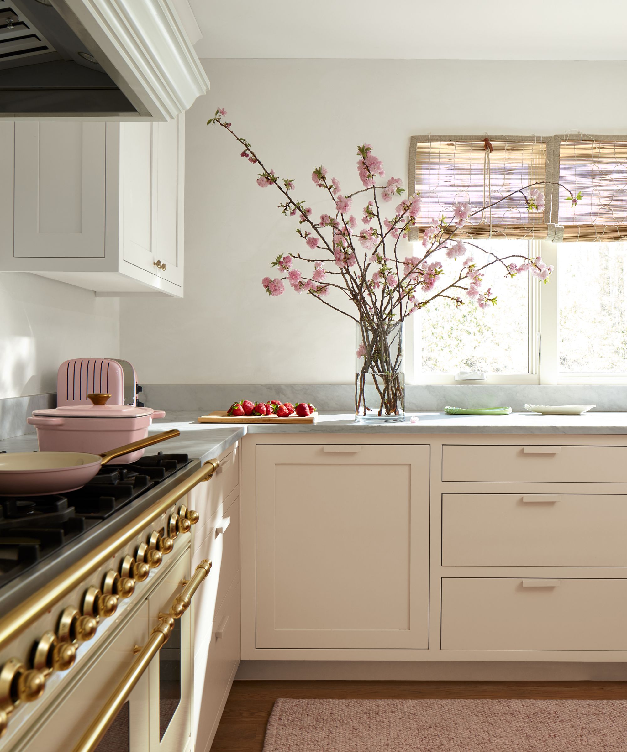 A small kitchen with pale pink cabinets, gray countertops, and warm white walls