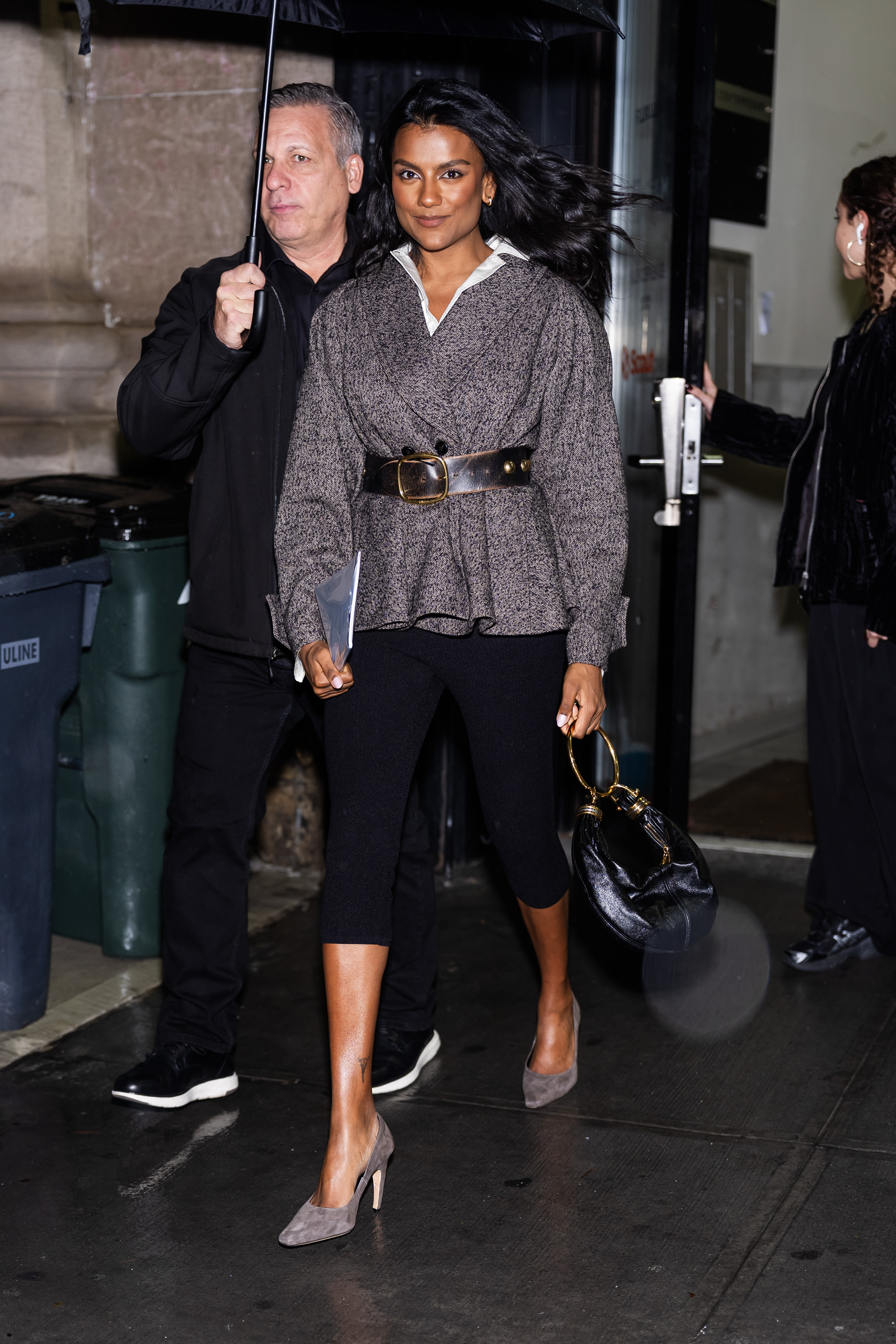 Simone Ashley walks outside in New York wearing black carpi leggings with a tweed belted jacket and mole suede heels.