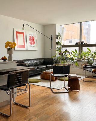 Shot of an open concept living room with hard wood floors and white walls. There is a black leather couch, black and metal accent chairs and a white area rug