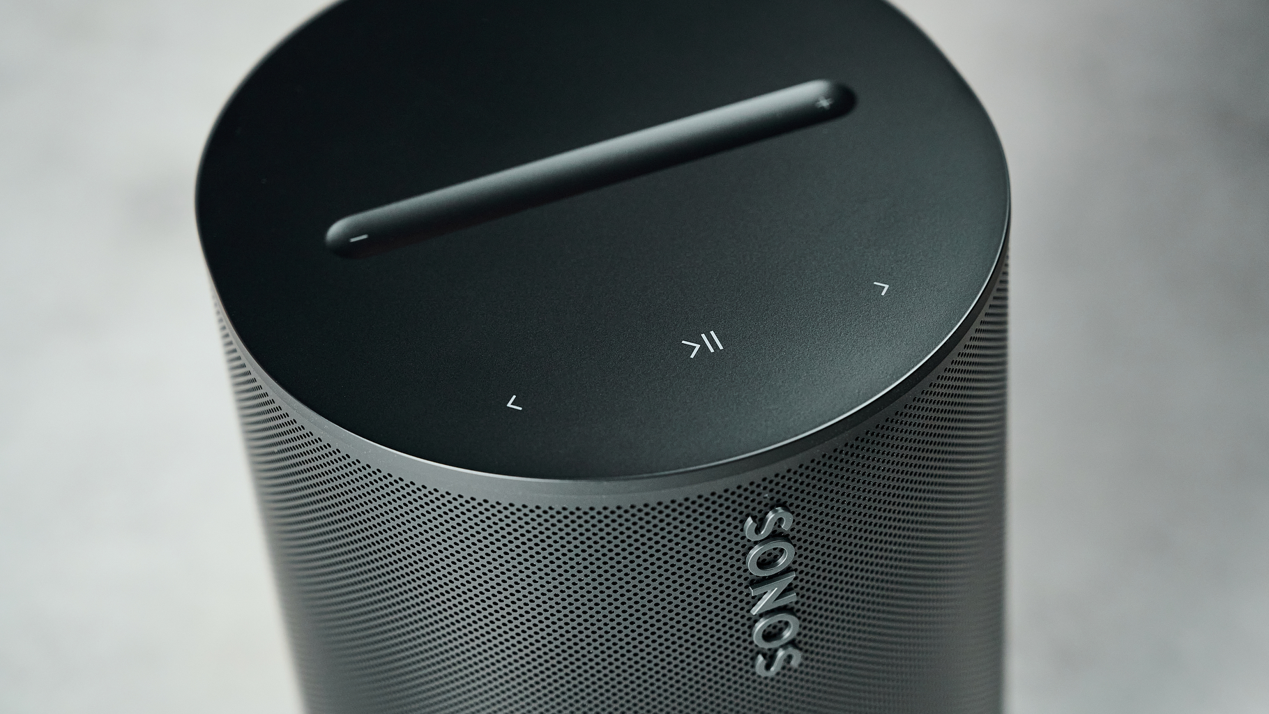 A closeup of the Sonos Era 100 SL from above, showing the play/pause and skip buttons and volume bar on top.